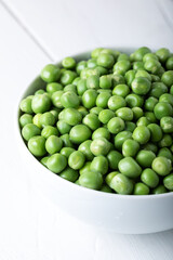 Green peas in white bowl with fresh pods on the wooden table. 