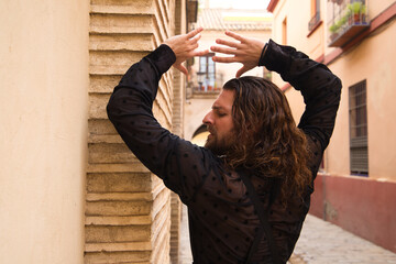 Long haired man dancing flamenco with black shirt and red roses. He makes dancing postures with his hands in a typical narrow street of Seville. Flamenco dance concept cultural heritage of humanity.