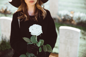 Sad woman in the cemetery holding bouquet of roses in her hand
