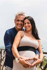 Happy couple with pregnant woman standing against a beautiful sea landscape during the summer...
