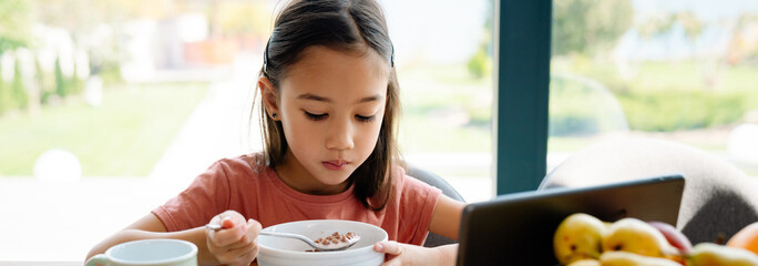 Asian girl using tablet computer while having breakfast