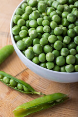 Green peas in white bowl with fresh pods on the wooden background.