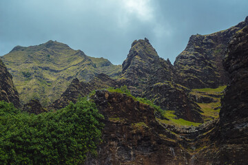 The gorgeous rugged wilderness and cliffs of Kauai's Napali Coast in Hawaii, with low clouds and mist hanging over the mountain peaks under a stormy grey sky