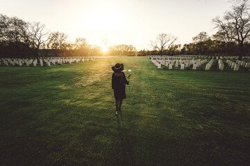 Sad woman in the cemetery holding bouquet of roses in her hand - Female grieving for a lost love -...