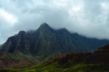 The gorgeous rugged wilderness and cliffs of Kauai's Napali Coast in Hawaii, with low clouds and mist hanging over the mountain peaks under a stormy grey sky