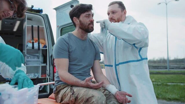 Two medics provide first aid to wounded soldiers screaming in pain near ambulance. Military concept. War. Outdoors
