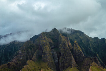 The gorgeous rugged wilderness and cliffs of Kauai's Napali Coast in Hawaii, with low clouds and mist hanging over the mountain peaks under a stormy grey sky