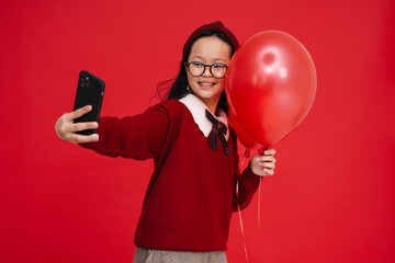 Asian preteen girl taking selfie on cellphone while posing with balloons