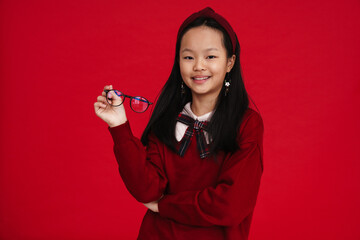 Asian preteen girl wearing headband smiling and holding eyeglasses