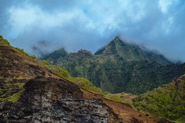 The gorgeous rugged wilderness and cliffs of Kauai's Napali Coast in Hawaii, with low clouds and mist hanging over the mountain peaks under a stormy grey sky