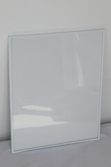 Large white photo frame on the floor, mockup, poster on the wall, light background