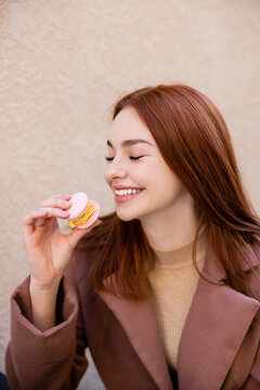 happy young woman with red hair holding sweet macaron.
