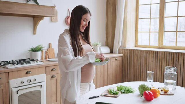 Cheerful pregnant woman tastes slice of cucumber in salad