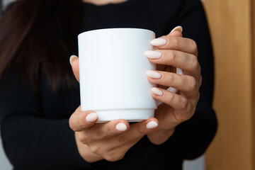 White mug for tea and coffee in the hands of a girl, close-up