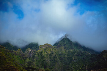 The gorgeous rugged wilderness and cliffs of Kauai's Napali Coast in Hawaii, with low clouds and mist hanging over the mountain peaks under a stormy grey sky