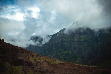 The gorgeous rugged wilderness and cliffs of Kauai's Napali Coast in Hawaii, with low clouds and mist hanging over the mountain peaks under a stormy grey sky