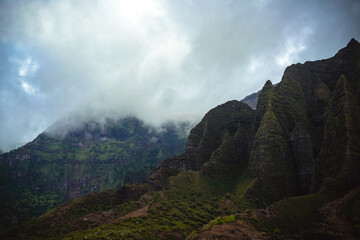 The gorgeous rugged wilderness and cliffs of Kauai's Napali Coast in Hawaii, with low clouds and mist hanging over the mountain peaks under a stormy grey sky