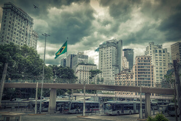 Sao Paulo Brazil city skyline seen from the city center bus station with the Brazilian flag waving in the background, in a cloudy day - obrazy, fototapety, plakaty