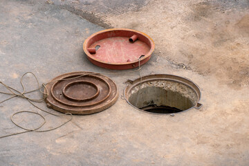 An open round hatch in the ground and metal hatch covers lying nearby. Underground engineering works. Repair and construction of underground sewers.