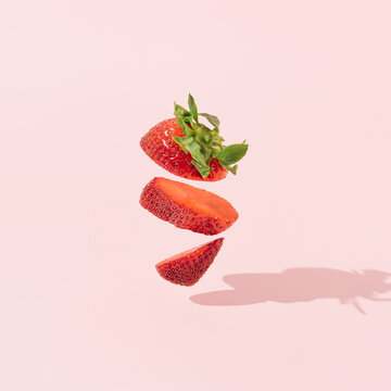 Levitating red strawberry slices with sunshine shadow against bright pink background. Minimal fruits concept. Summer or spring party food creative composition. Fun trendy idea.