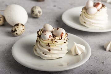 Meringue desserts topped with quail eggs and chocolate shavings on a gray background.