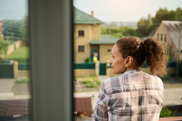 Close-up of a Hispanic woman in checkered shirt and denim shorts on her balcony