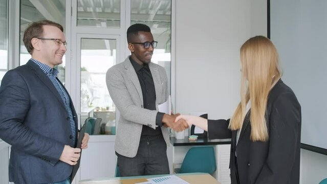 Business meeting of international multinational coworkers team finishing, all partners stand up and make handshake shaking their hands. Multiethnic top managers of company meet in office.