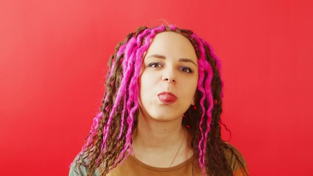 Young female with dreadlocks looking at camera and showing tongue. Funny woman aping on red background.