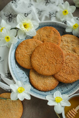 Fototapeta na wymiar Honey cookies with natural patterns on a plate on a dinner table with flowers and tea. Food photography in light colors with cookies and spring daffodils.