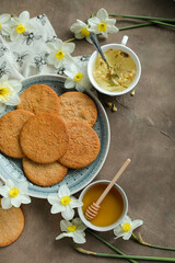 Honey cookies with natural patterns on a plate on a dinner table with flowers and tea. Food photography in light colors with cookies and spring daffodils.