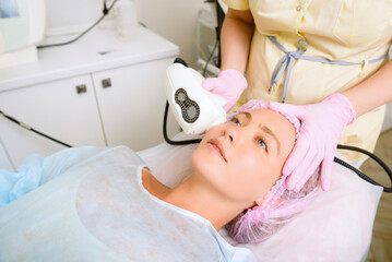 Image of a young beautiful woman dressed as a patient, lying on a couch in a cosmetology clinic.