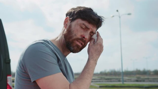 Close up wounded military man sitting touch face with blood near an ambulance. Medic. Military concept. War. Outdoors