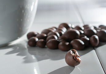 chocolate covered raisins, hazelnuts, coffee beans, almonds pouring out of a white bowl on a white...