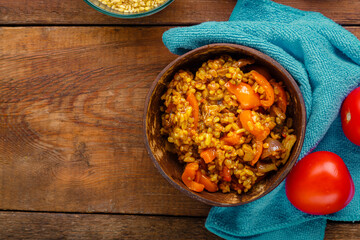 A plate of bulgur with vegetables and mushrooms on a blue napkin next to tomatoes on a wooden table.
