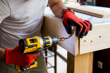 Man building a wooden table with a cordless electric screwdriver - obrazy, fototapety, plakaty