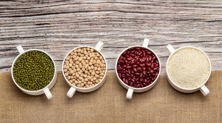 Top view of mung beans, kidney beans, rice and chickpeas  in bowls  on wooden background covered with burlap