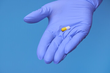 hand in medical blue gloves hold capsules of medicine for covid 19