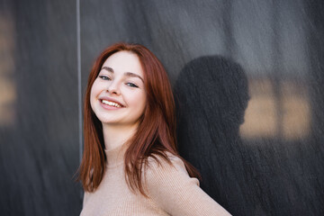Fototapeta na wymiar happy redhead woman in beige turtleneck smiling near grey marble wall.