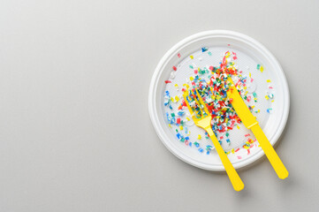 Microplastic in white plastic dish with knife and fork. Light grey background. Microplastic problem concept. Overhead view with place for text