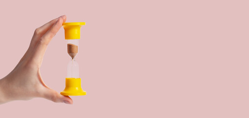 Banner with woman hand holding sand clock on pastel background. Time, punctuality concept. Device for measuring one minute passage. Space for text. High quality photo