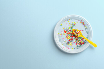 Microplastic in white plastic dish with spoon. Pastel blue background. Microplastic problem concept. Overhead view with place for text