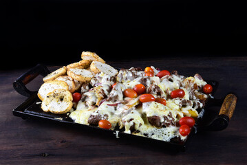 roast beef on iron plate with cheese, tomato pepper herbs, onion, cassava and bread