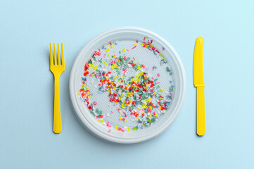 Microplastic in white plastic dish with knife and fork. Pastel blue background. Microplastic problem concept. Overhead view