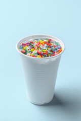 Microplastic in white plastic cup with water. Pastel blue background. Microplastic problem concept.