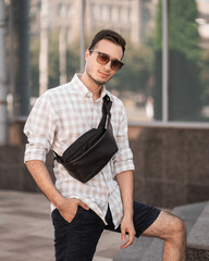 portrait of a young handsome man in glasses with a bag on his chest and a checkered shirt