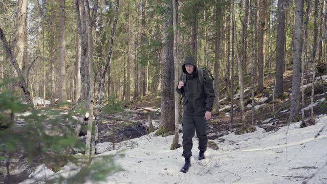 A male traveler travels with a backpack through a pine forest, walks through the snow in a spring forest. Slow motion