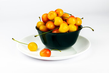 Ripe sweet rainier cherries in a  bowl and on plate on white background.