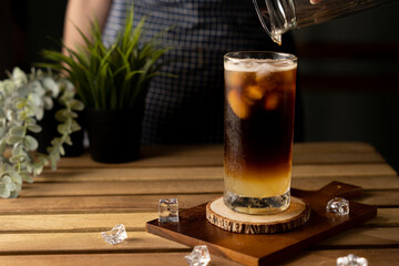 Glass of espresso with lemon juice on wooden table and copy space, Summer Cocktail, Cold brew coffee or black tea. (close up, selective focus),Pouring cold drink.