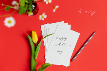 
Mother's Day message with flowers and candies. Congratulations on mother's day with a card and spring flowers yellow tulip on a red flat lay background.