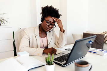 Beautiful young businesswoman sitting alone in her home office and suffering from a headache. Young businesswoman experiencing fatigue during her work day. Tired businesswoman suffering from headache.